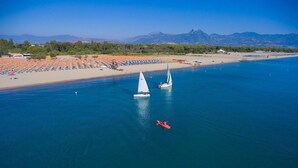 Zona costera con playa, barcos y montañas al fondo.