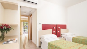 Habitación de hotel con dos camas, un escritorio con silla, un armario rojo y vistas al exterior.