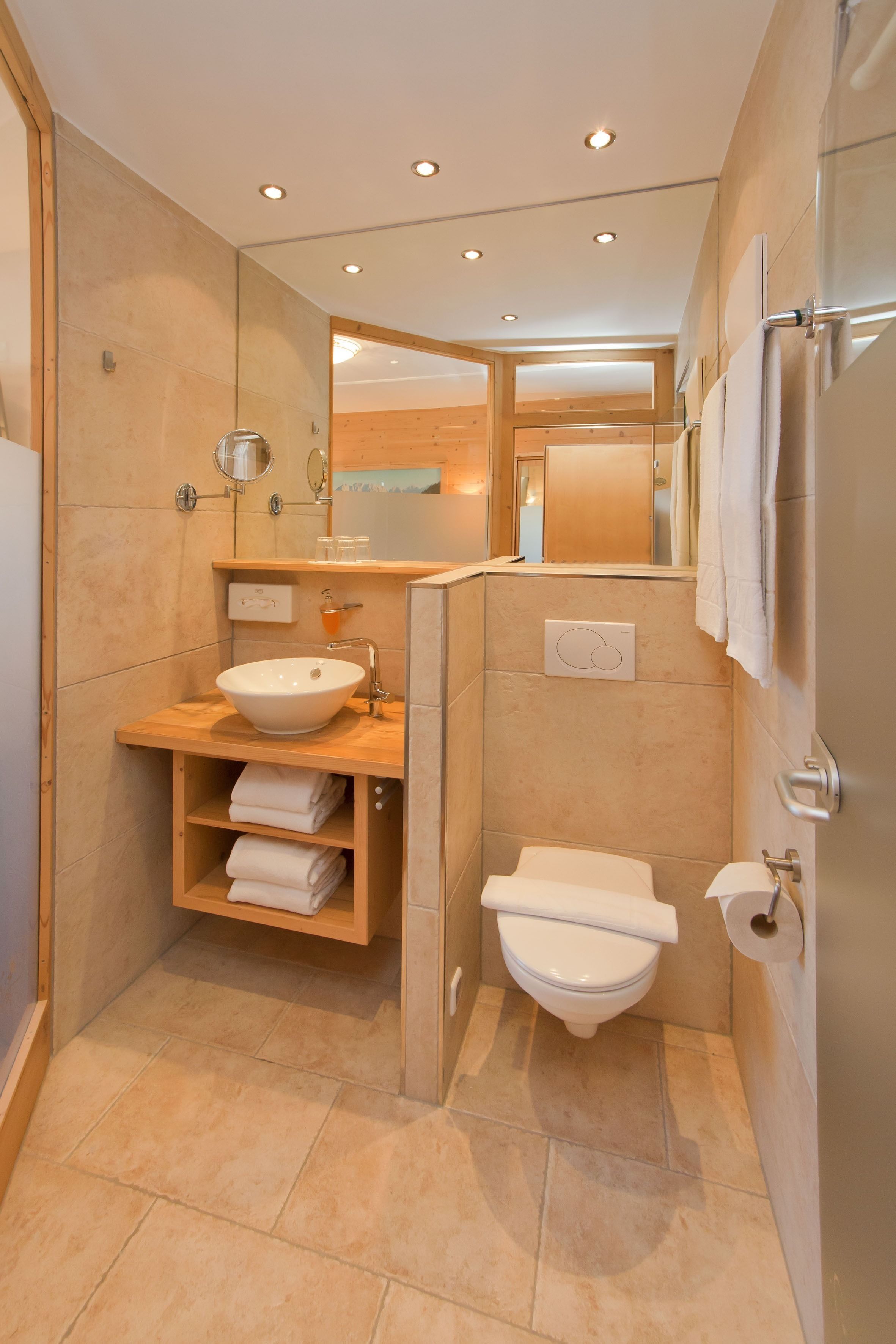 Un bagno moderno con un mobile bagno in legno, un lavandino bianco, un water e una cabina doccia in vetro.