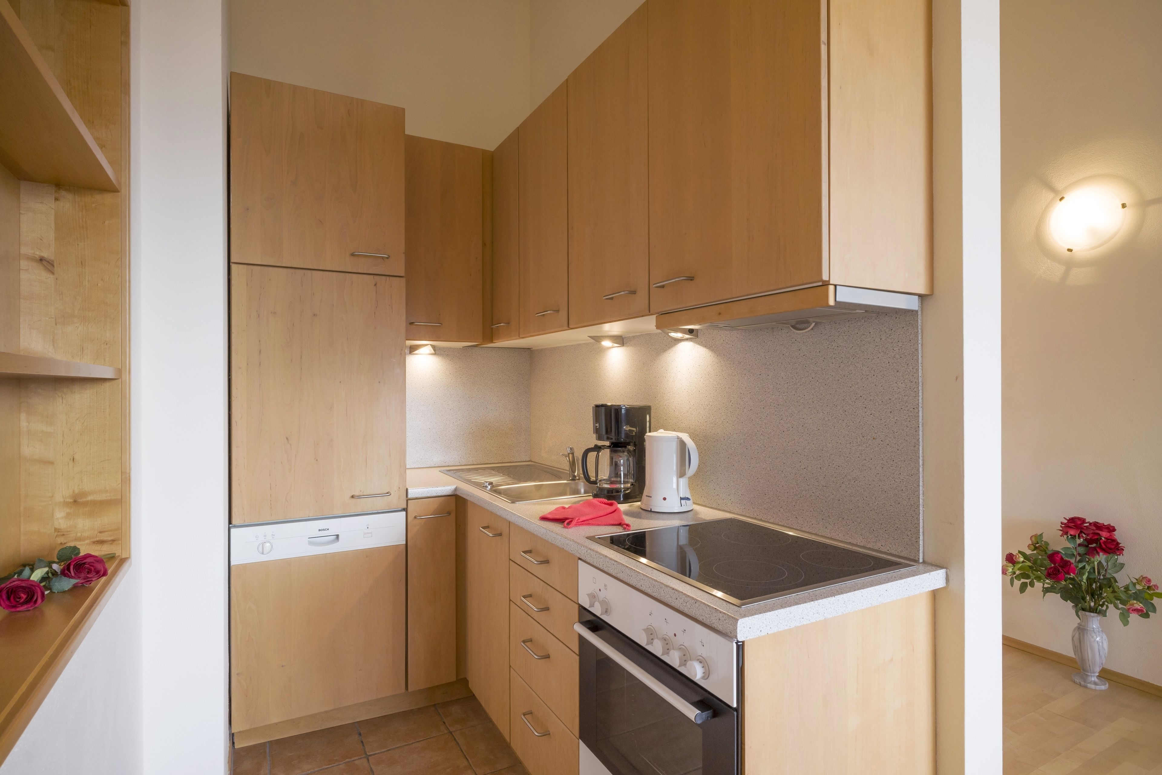 A compact kitchen with wooden cabinets, a built-in oven, and a coffee maker.