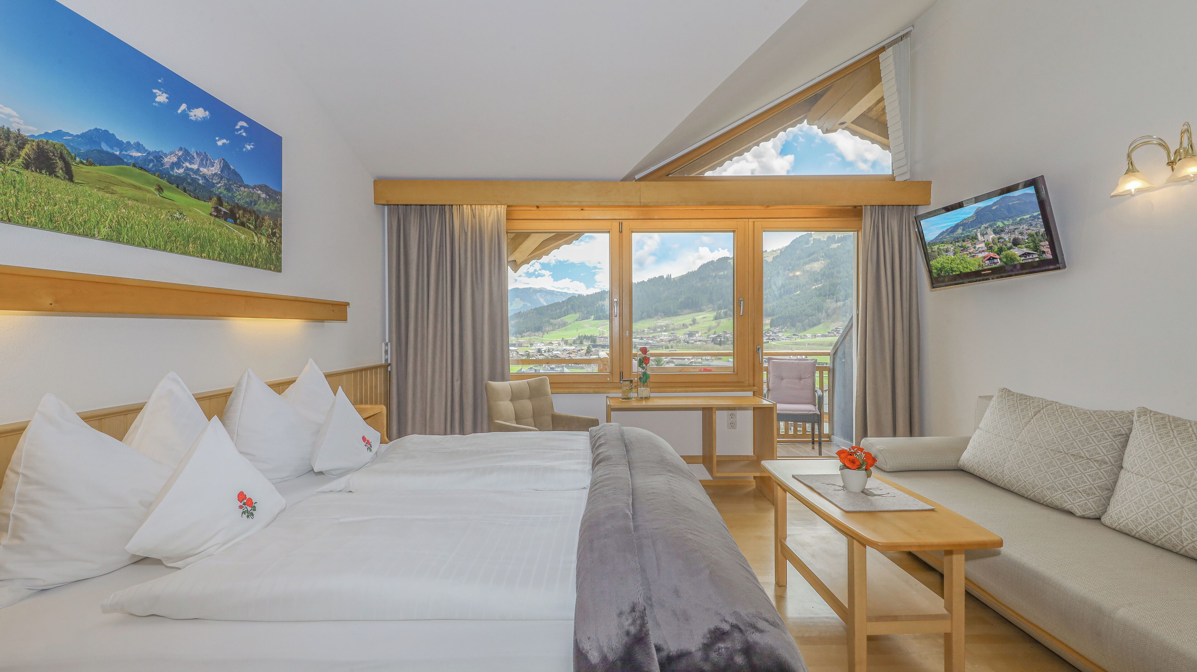 A hotel room with a bed, a sofa, a small table, and a TV.