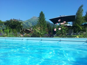 A swimming pool with clear blue water, surrounded by lush greenery and flowers. - Gartenhotel Rosenhof Kitzbuehel (Oberndorf in Tirol)