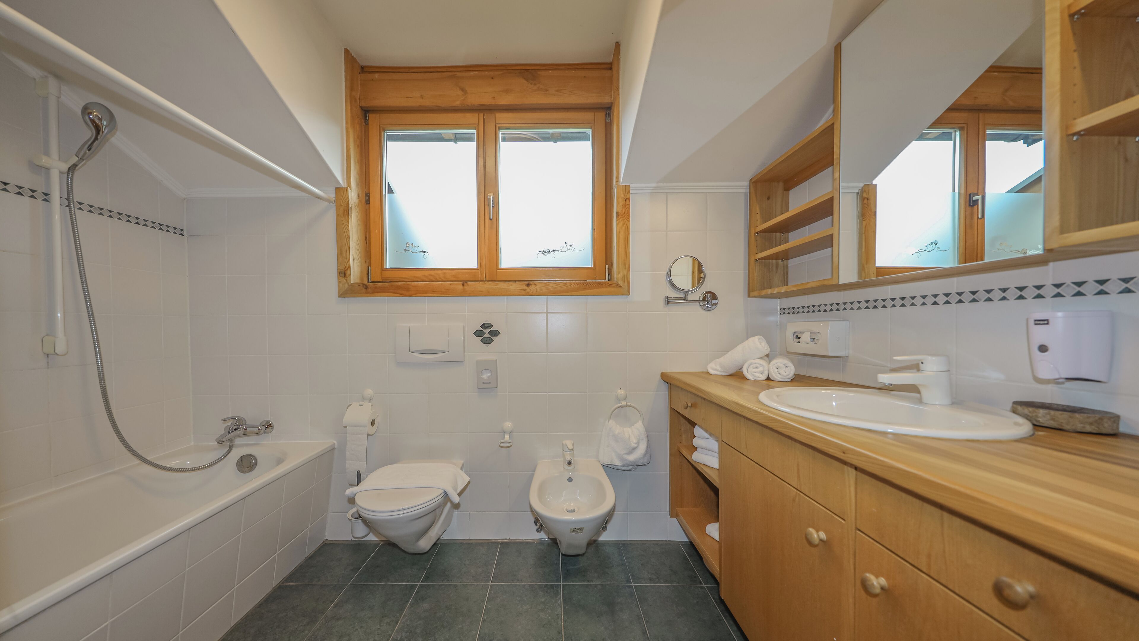 Une salle de bain avec une baignoire, deux toilettes, un lavabo et un meuble-lavabo en bois.