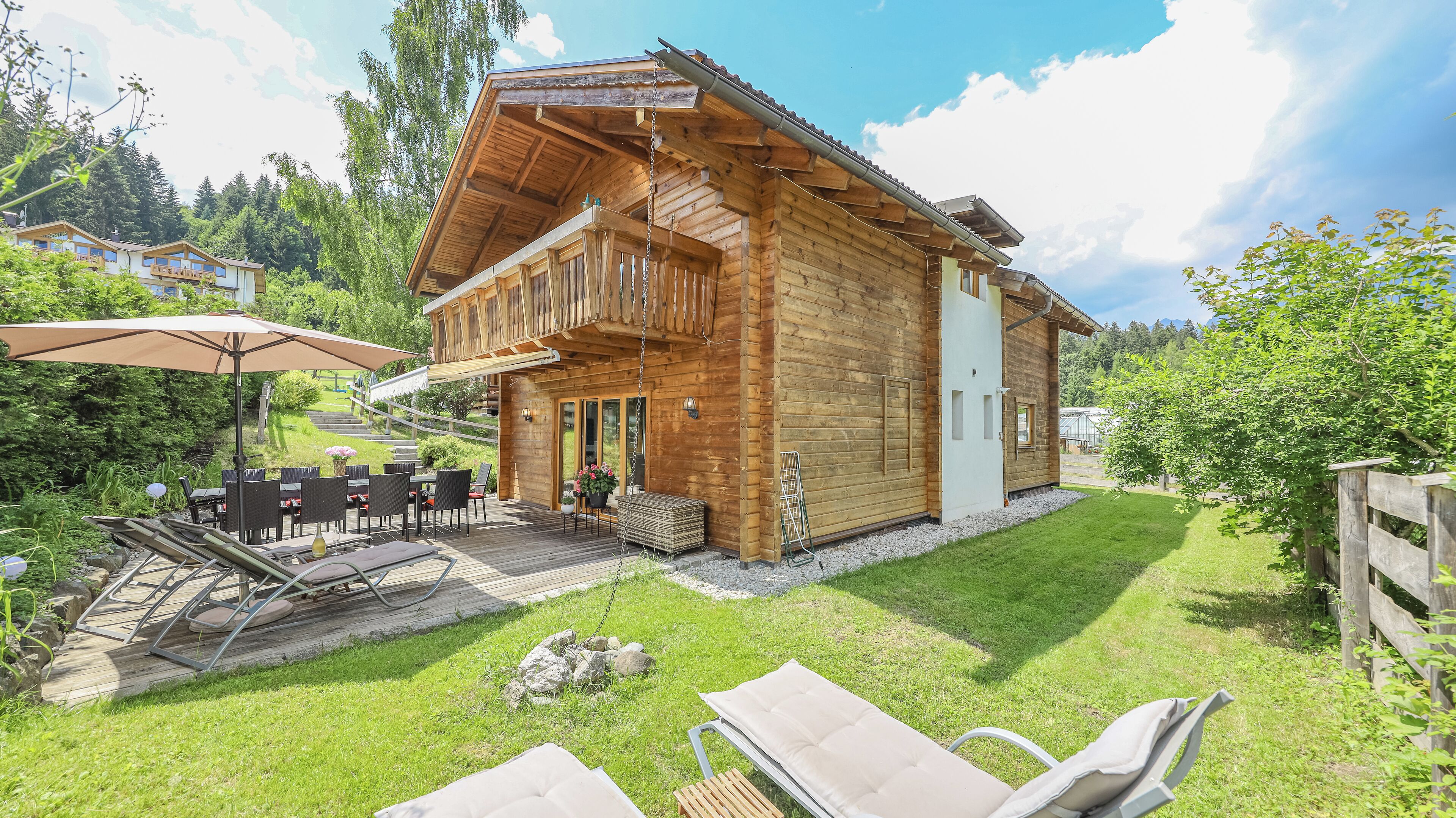 A wooden chalet with a balcony, outdoor seating, and a view of the surrounding greenery.