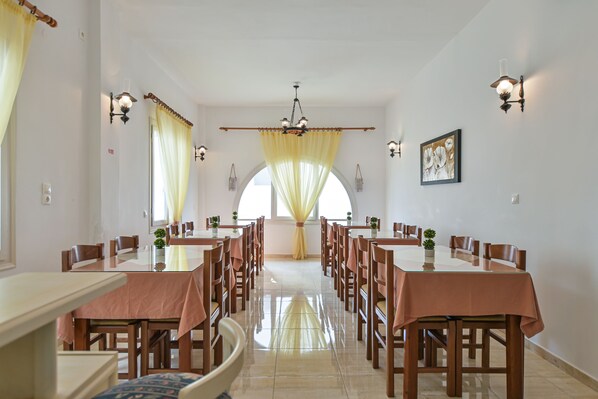 A dining area with multiple tables and chairs, a chandelier, and wall sconces.