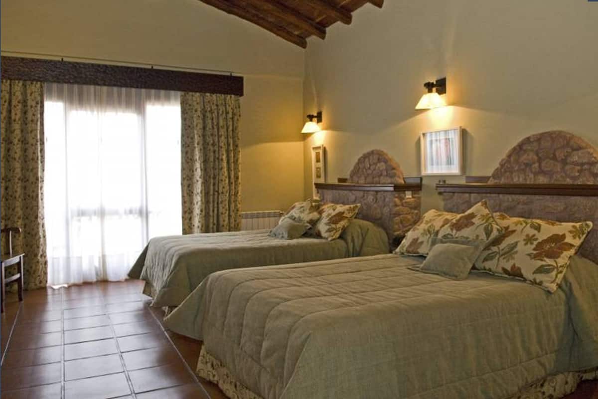 A room with two beds, a stone fireplace, and a window with curtains.