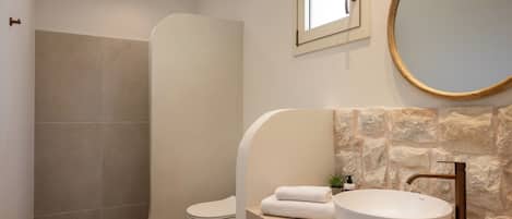 Une salle de bain avec une douche à parois courbes, des toilettes, un lavabo avec un receveur rond et un mur en pierre.