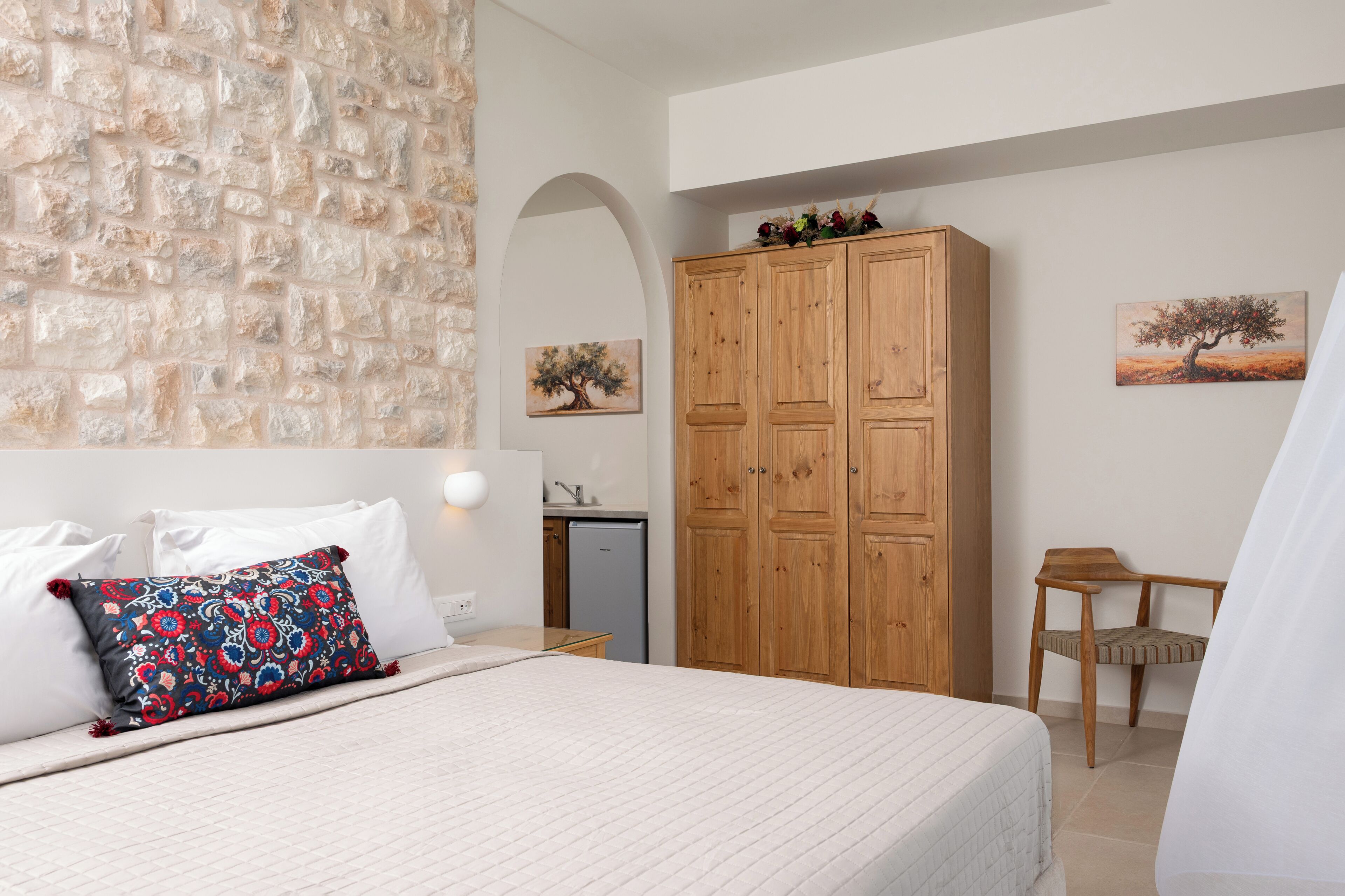 Un dormitorio con cama, un armario de madera, una mesita, una silla y una pared con diseño de piedra y dos cuadros.