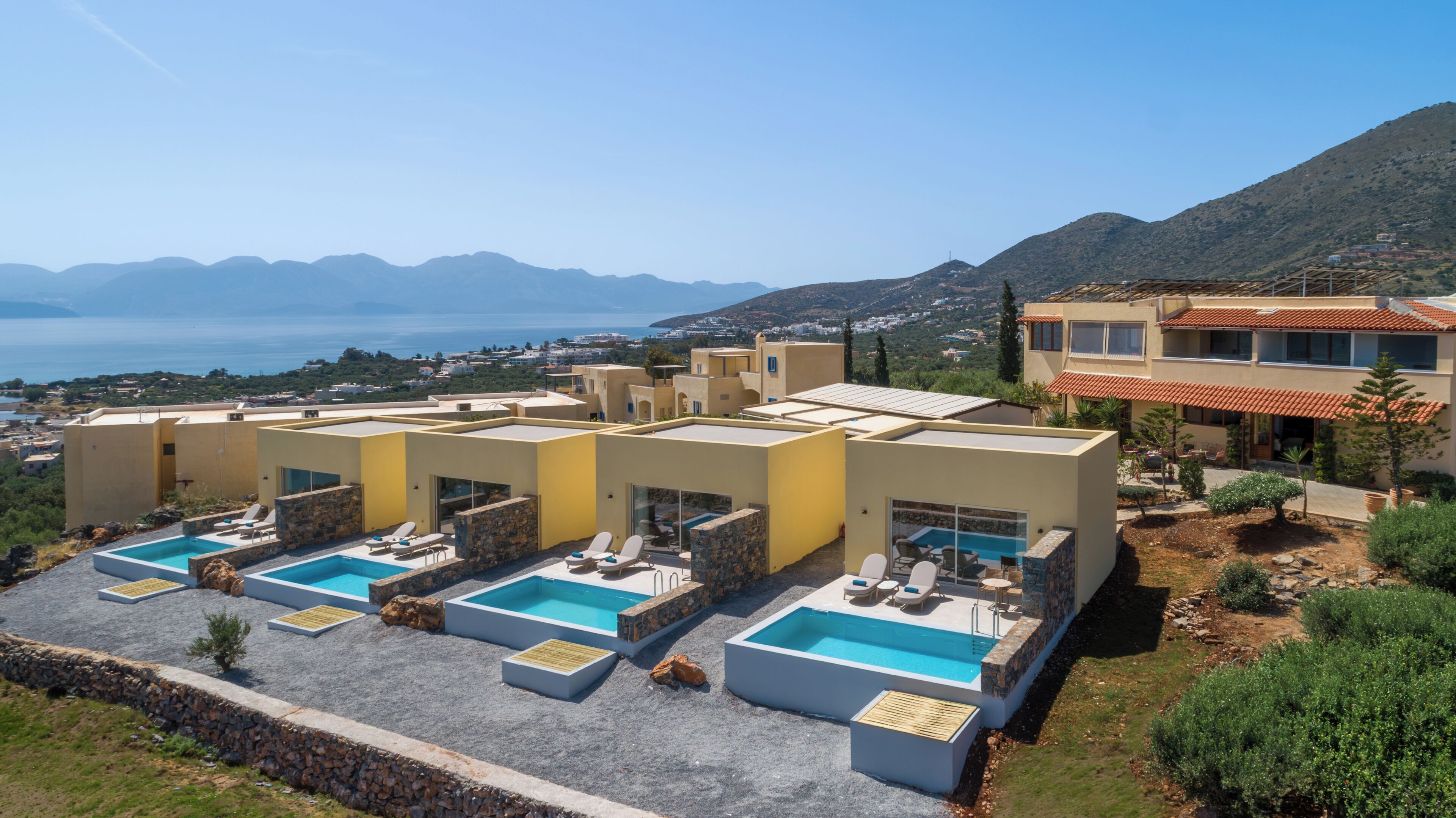 A resort with multiple swimming pools, a view of the sea, and a mountainous backdrop.