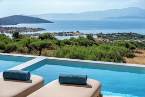 Une piscine avec deux chaises longues, une serviette et une vue sur la mer et les collines.