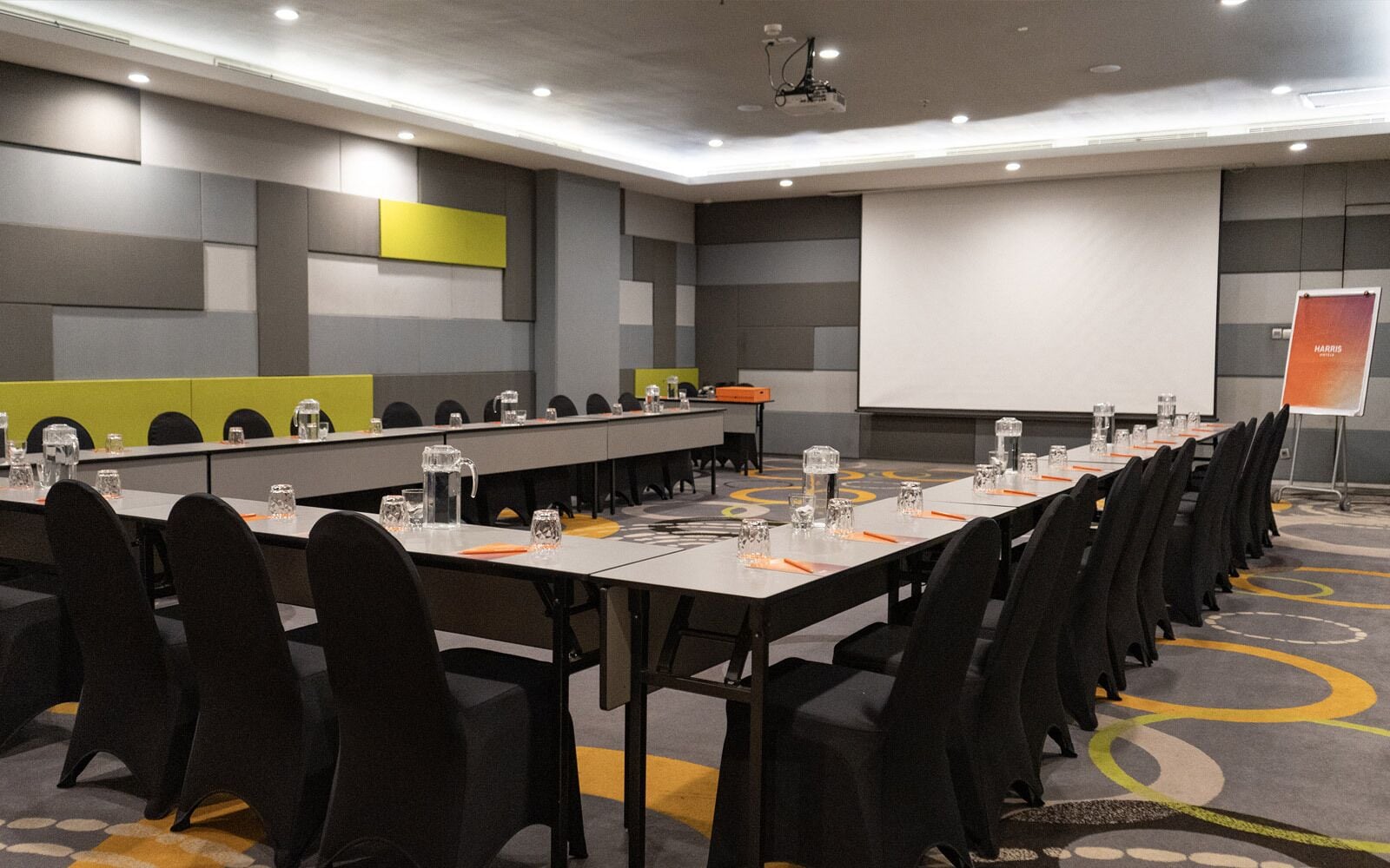 Une salle de conférence équipée de longues tables, de chaises et d’un écran de projection.