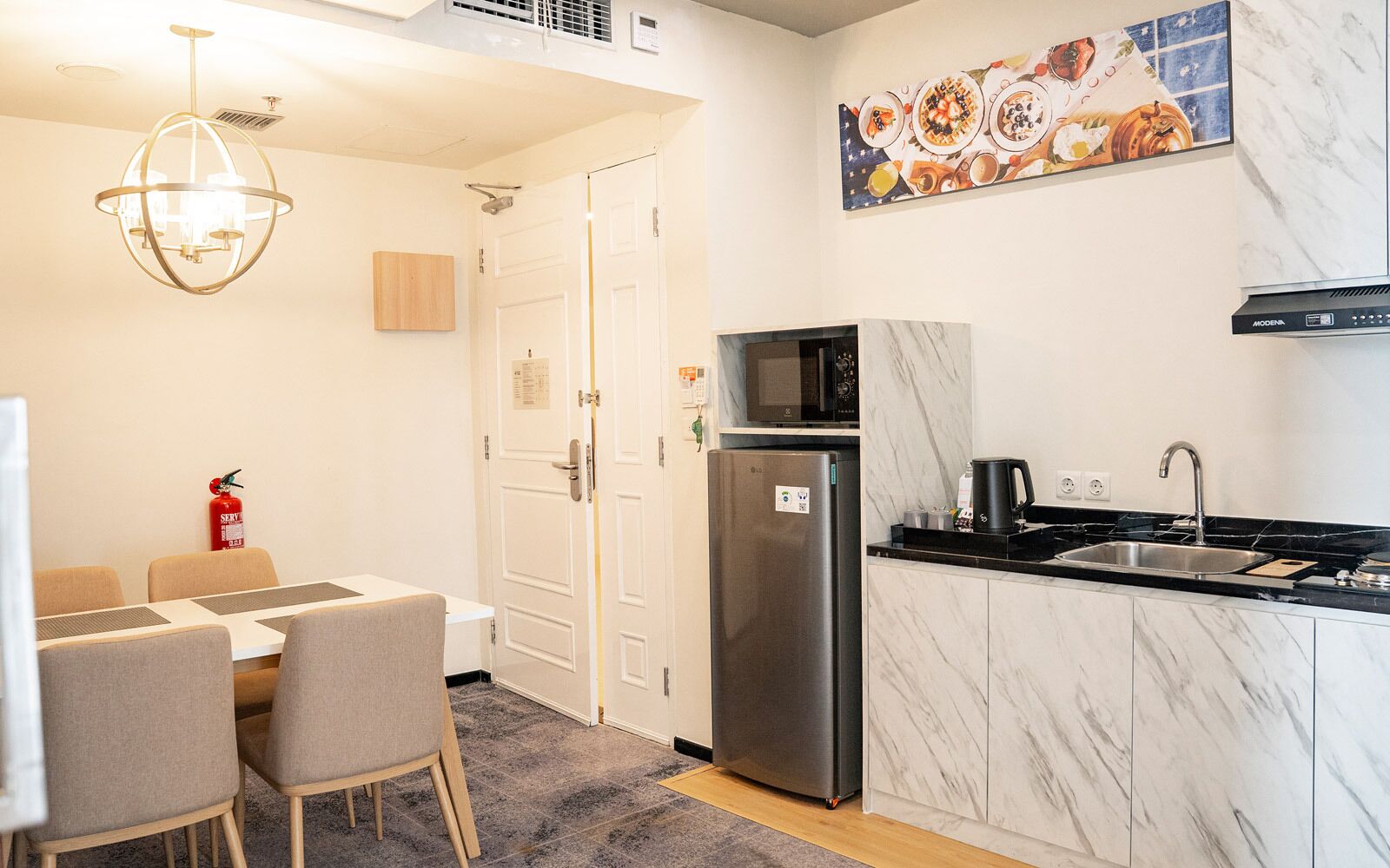 A compact kitchen with a refrigerator, microwave, and sink. There is a dining area with chairs and a table.