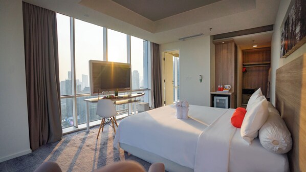 A hotel room with a large bed, a desk with a TV, and a view of the city. - HARRIS Suites FX Sudirman Jakarta (Jakarta)