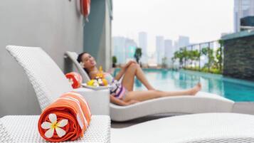 Un área de descanso junto a la piscina con una silla reclinable, una toalla con un estampado floral y una persona relajándose junto a la alberca.