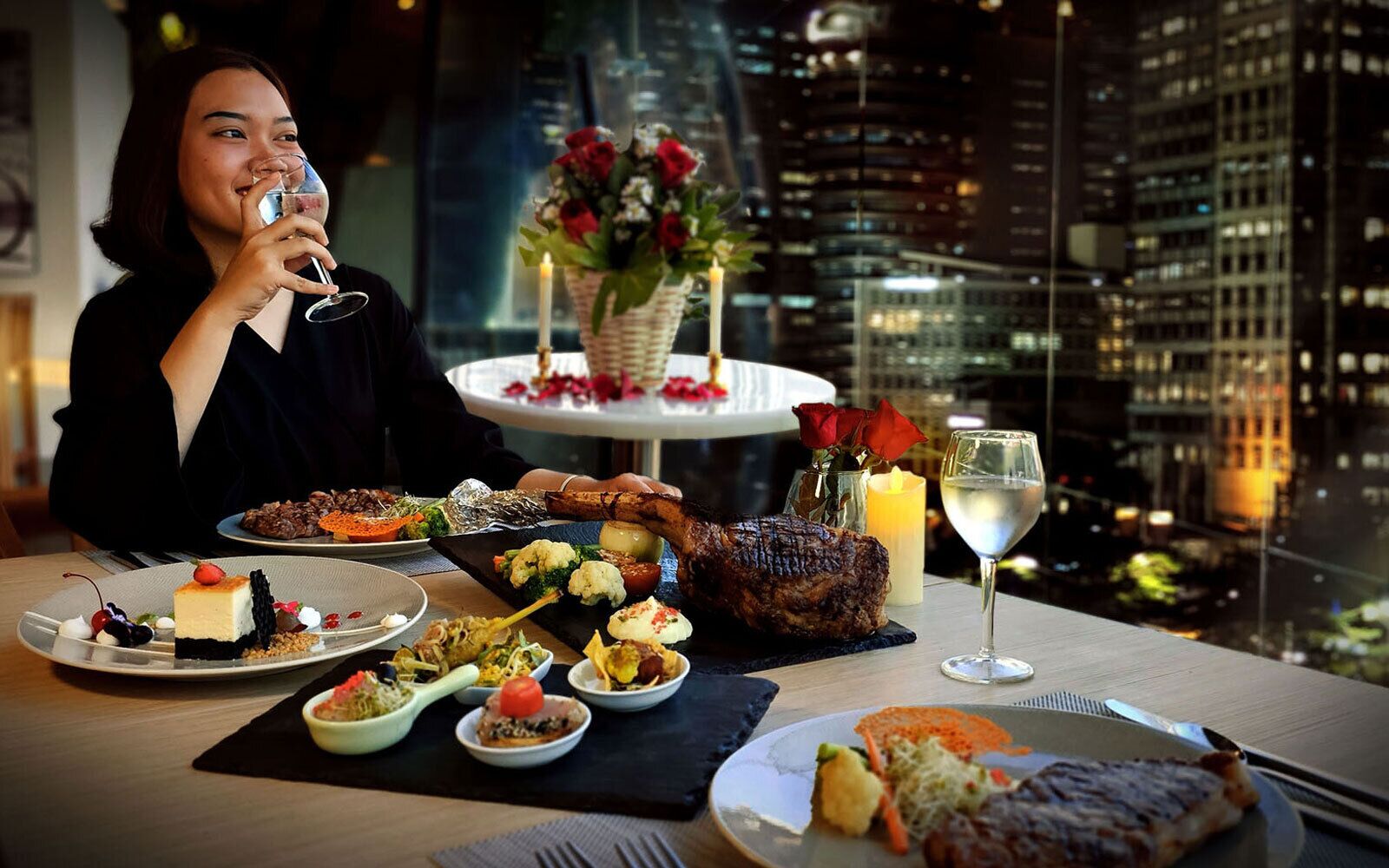 A dining table with various dishes, a candle, and a glass of white wine, set against a cityscape view.