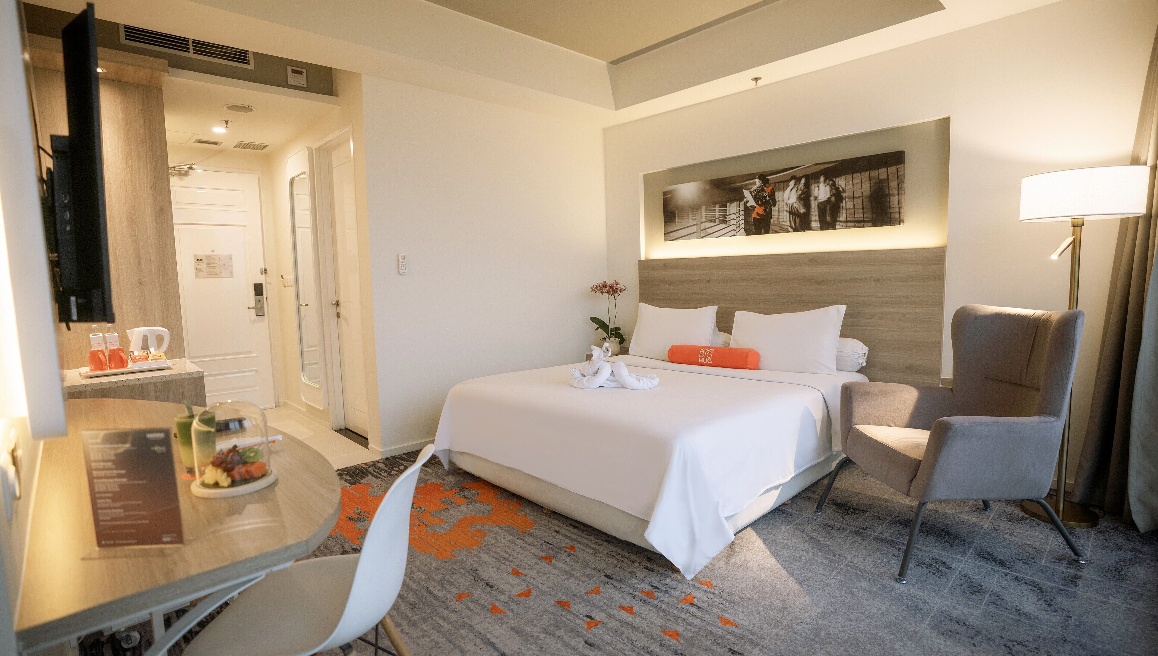 A hotel room with a bed, a desk, a chair, a lamp, and a painting on the wall.