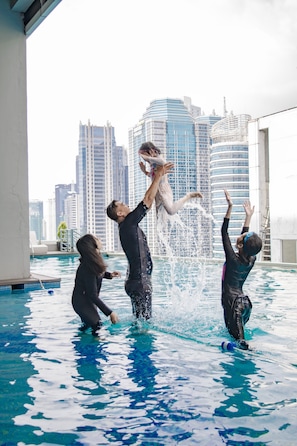 Um grupo de pessoas brincando em uma piscina, com um horizonte urbano ao fundo.