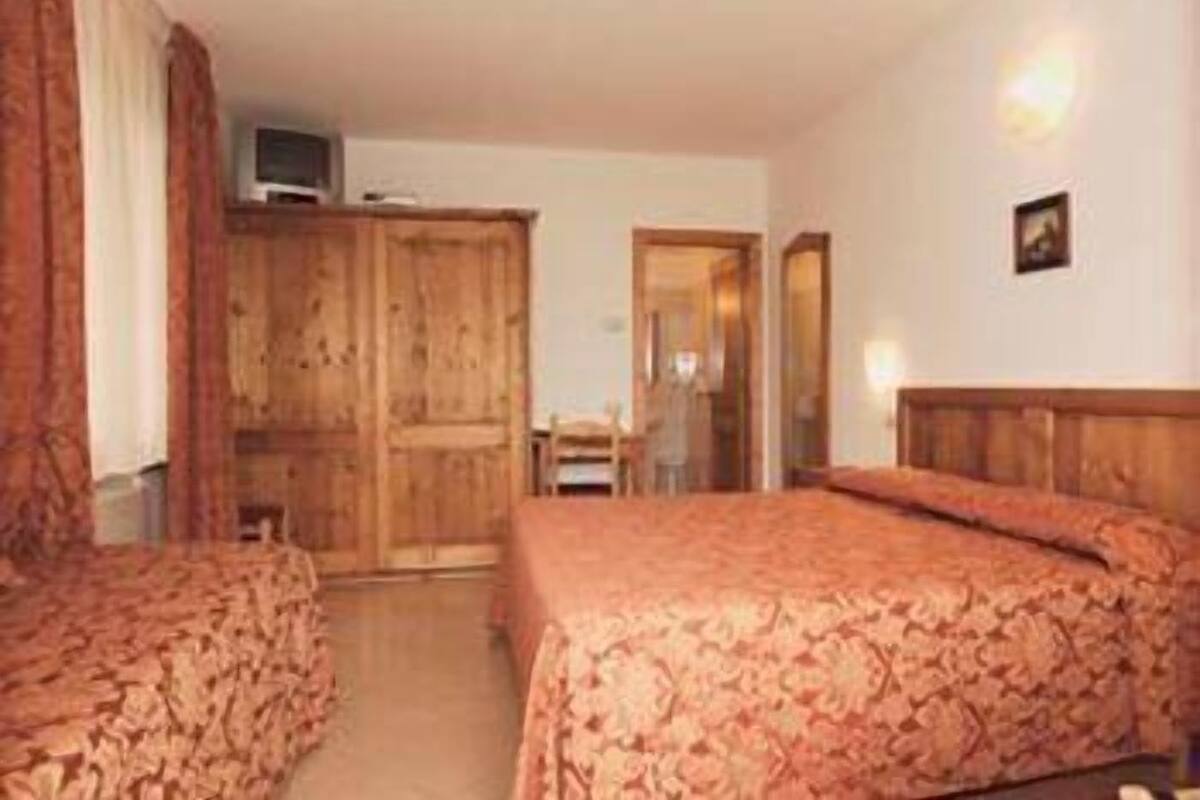 Habitación de hotel con dos camas, un armario de madera y un pequeño escritorio con silla.