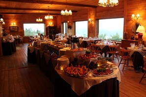 A dining area with multiple tables set for a meal, featuring a variety of dishes and a warm, wooden interior. - Pourvoirie du Cap au Leste (Sainte Rose du Nord)