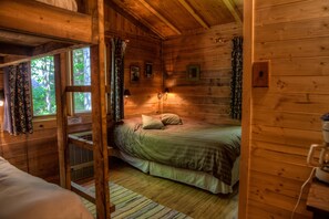 A wooden cabin bedroom with a bunk bed, a small table, and a window with curtains. - Pourvoirie du Cap au Leste (Sainte Rose du Nord)