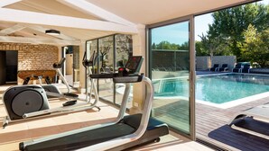 A home gym with exercise equipment and a view of a swimming pool. - Hotel Carcarille - Restaurant le C (Gordes)