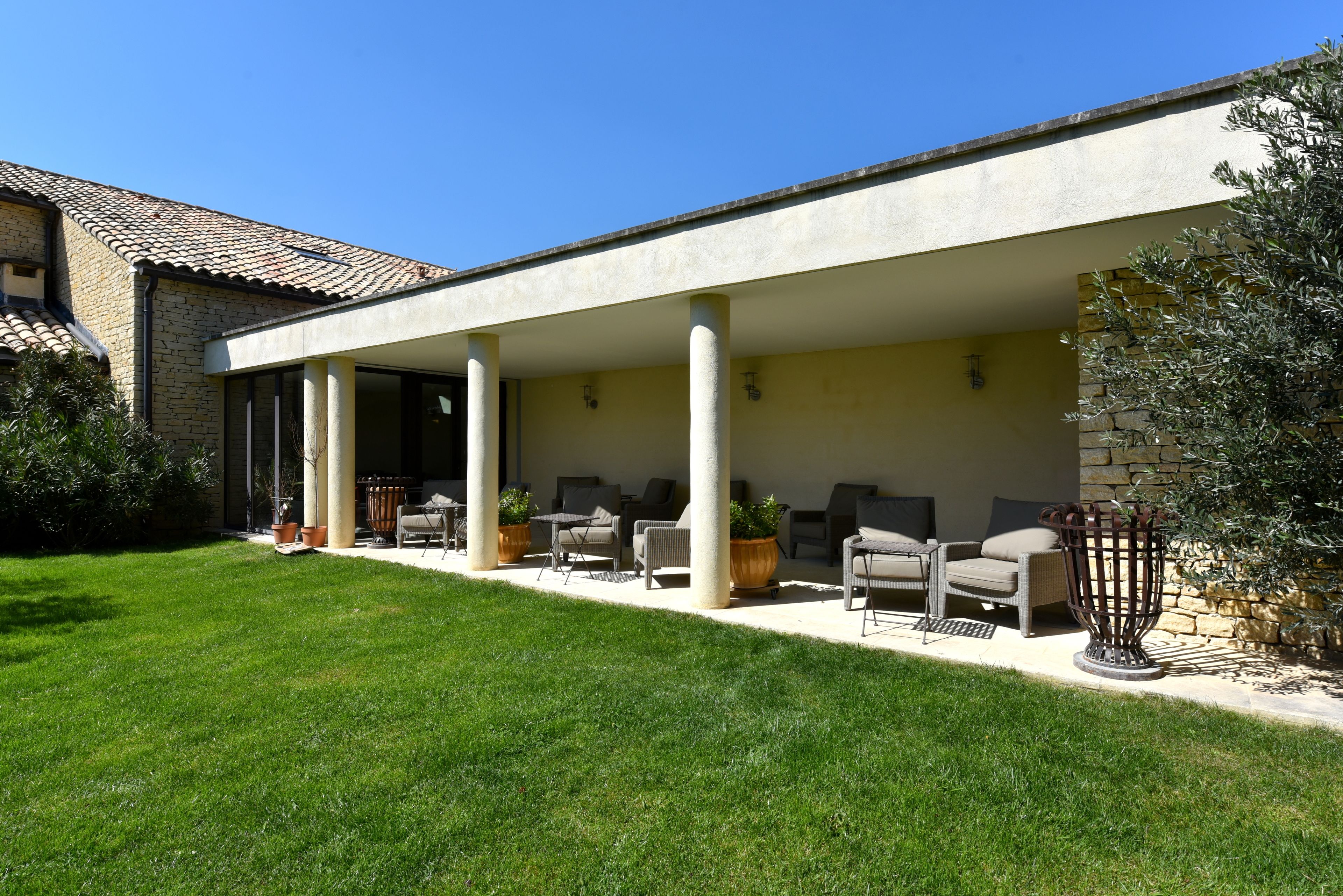 A covered outdoor patio with seating and planters, a stone wall, and a clear blue sky.