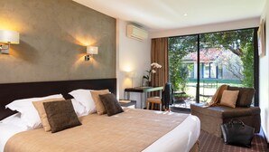 A hotel room with a large bed, a desk, a chair, and a view of the outdoors. - Hotel Carcarille - Restaurant le C (Gordes)