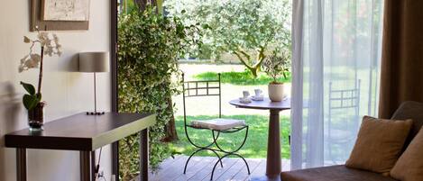 A room with a bed, a table with a plant, a chair, and a view of a garden through a glass door.
