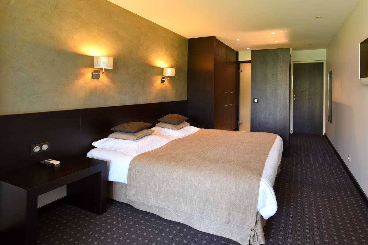 A hotel room with a large bed, bedside tables, a desk, and a wardrobe.