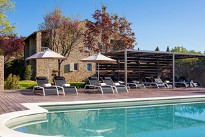A pool area with lounge chairs and umbrellas, a stone building, and a pergola.
