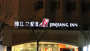 Exterior del Jinjiang Inn con un letrero llamativo, entrada de vidrio y un área de recepción acogedora con escalones y plantas en macetas.