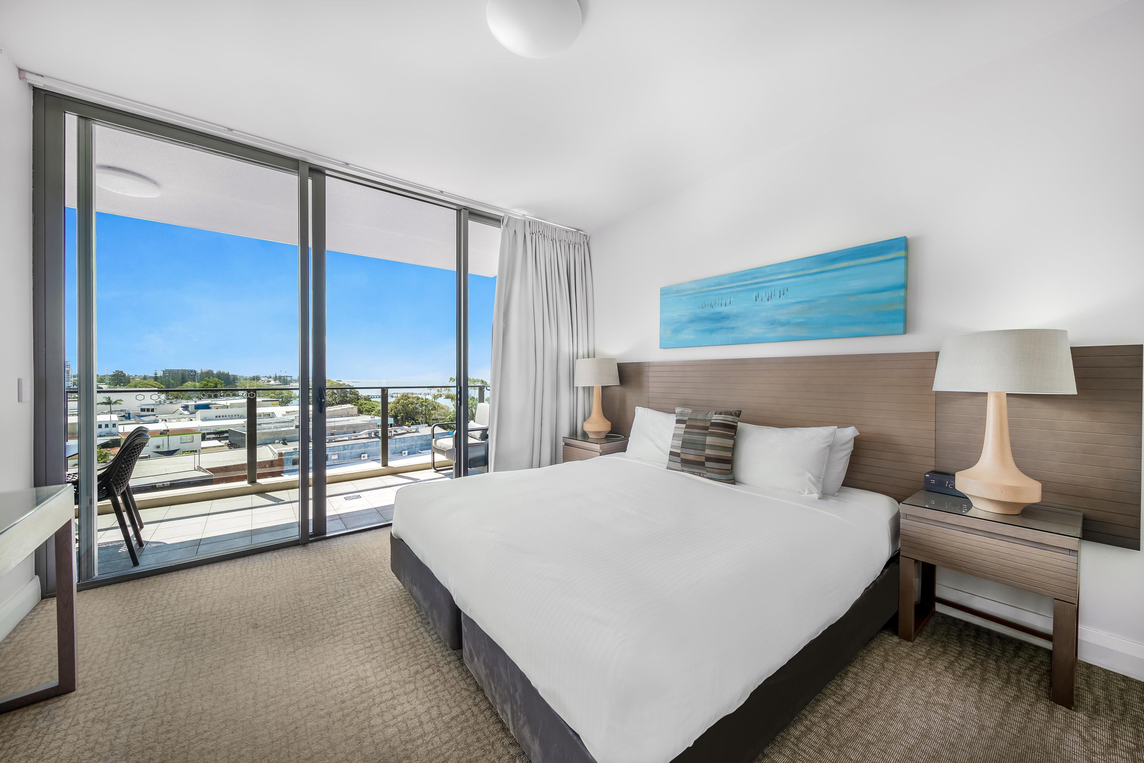 Habitación de hotel con una cama grande, un escritorio, una silla y vistas a una piscina y edificios.