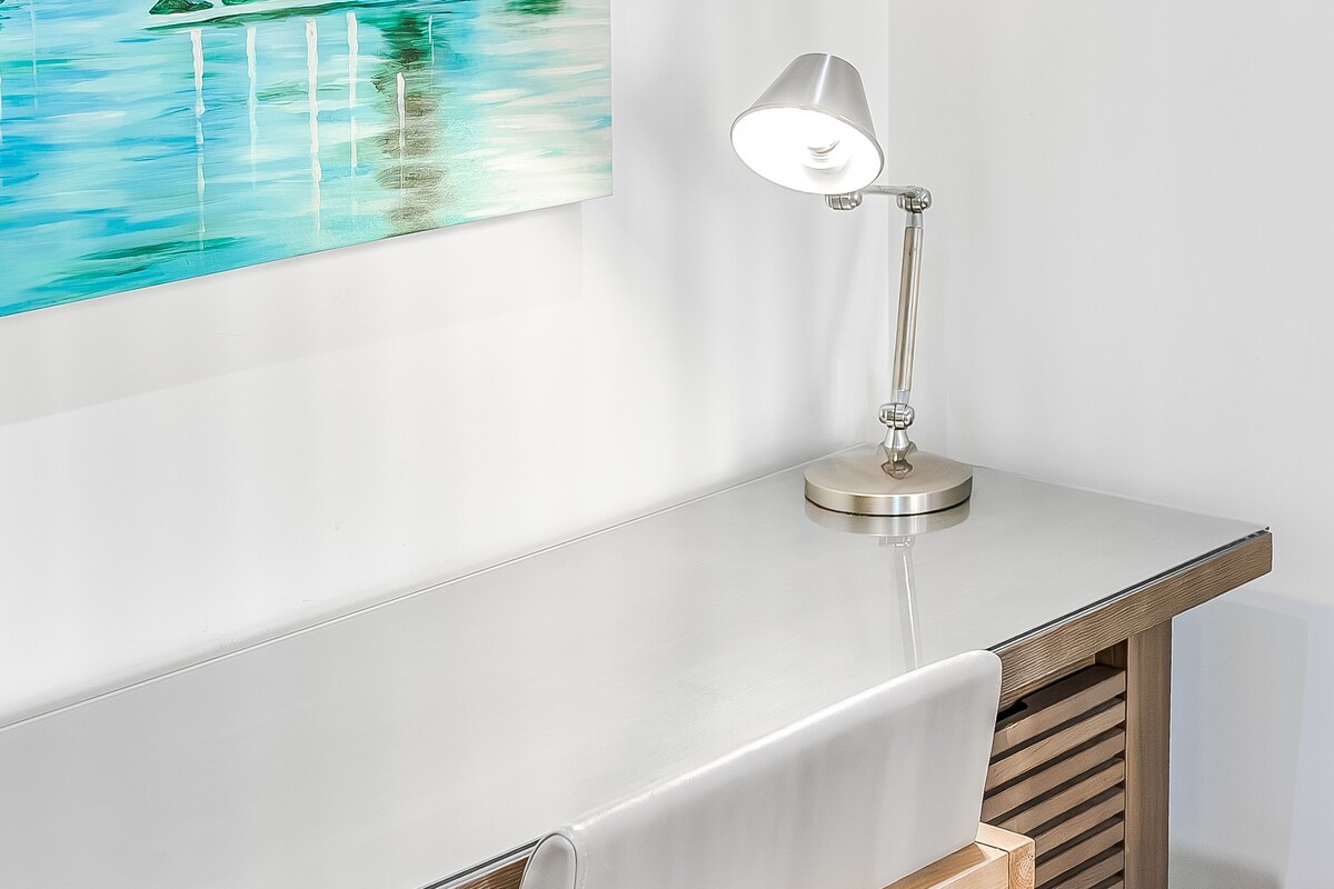 A desk with a lamp, a wooden slat bench, and a painting of a beach scene.