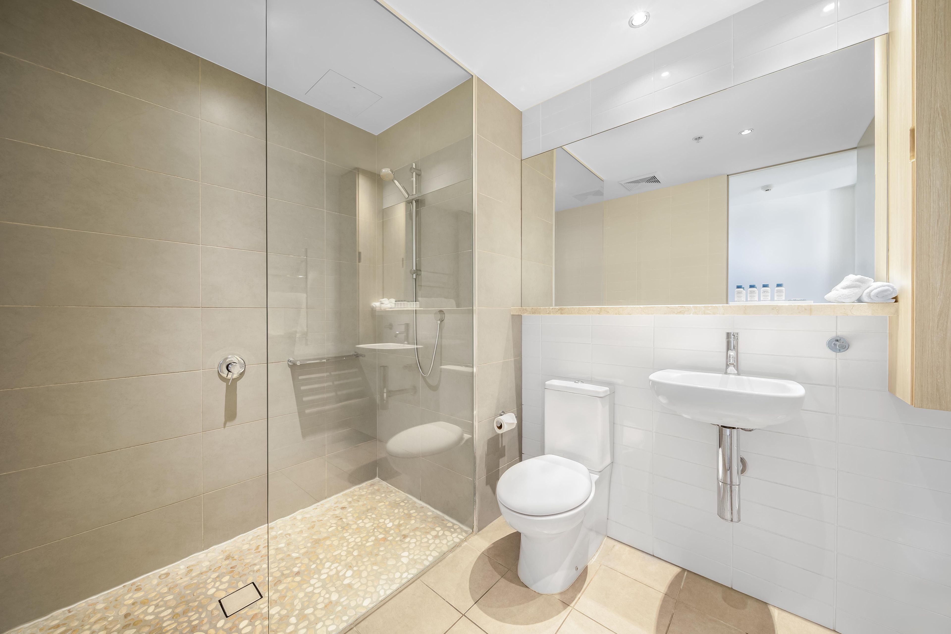Een moderne badkamer met een douchecabine van glas, een wit toilet en een wastafel met spiegel.