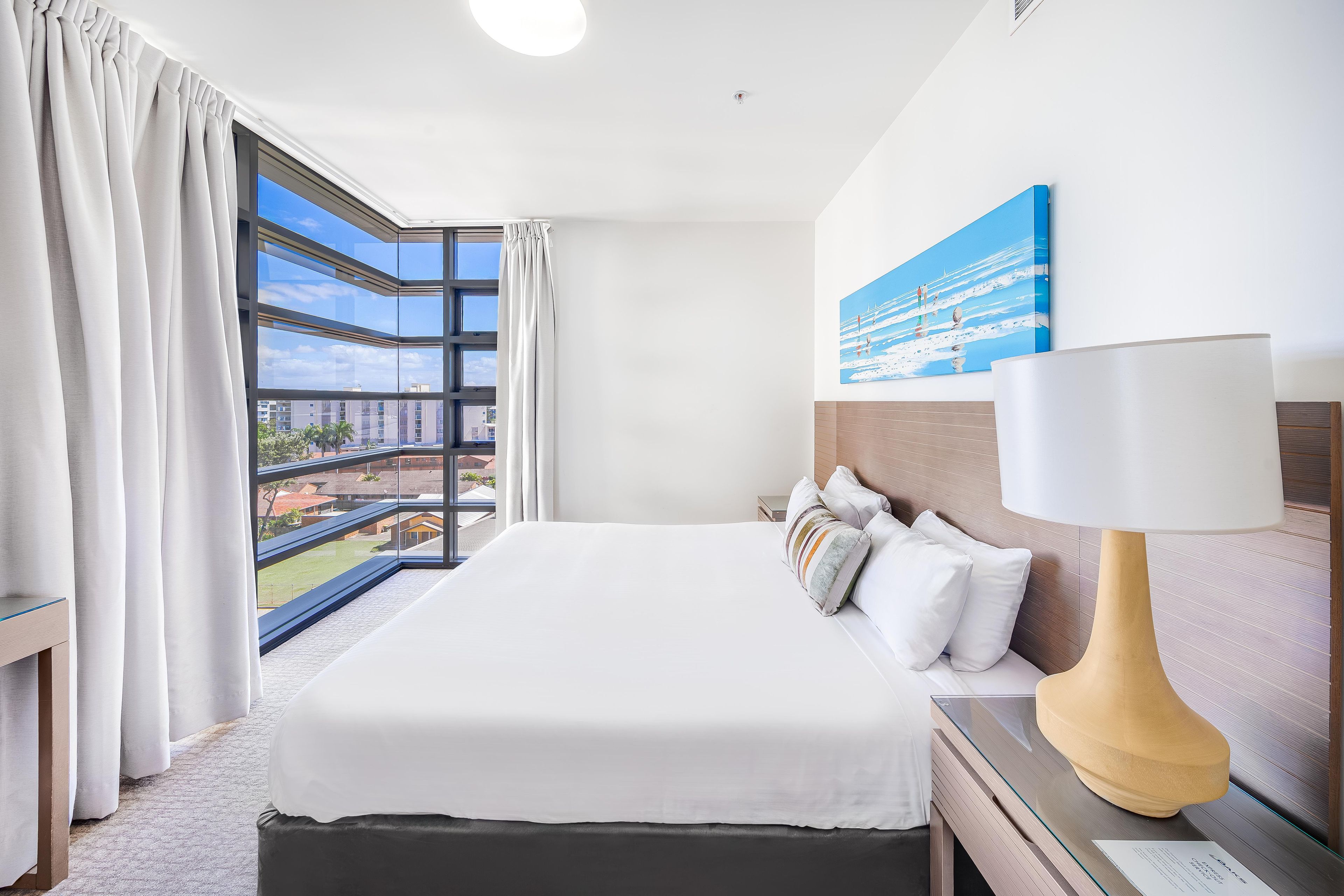 Una habitación de hotel con una cama grande, una mesita de noche, una lámpara y un cuadro en la pared.
