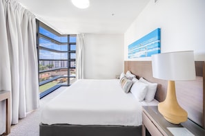 A hotel room with a large bed, a nightstand, a lamp, and a painting on the wall. - Oaks Redcliffe Mon Komo Suites (Redcliffe)