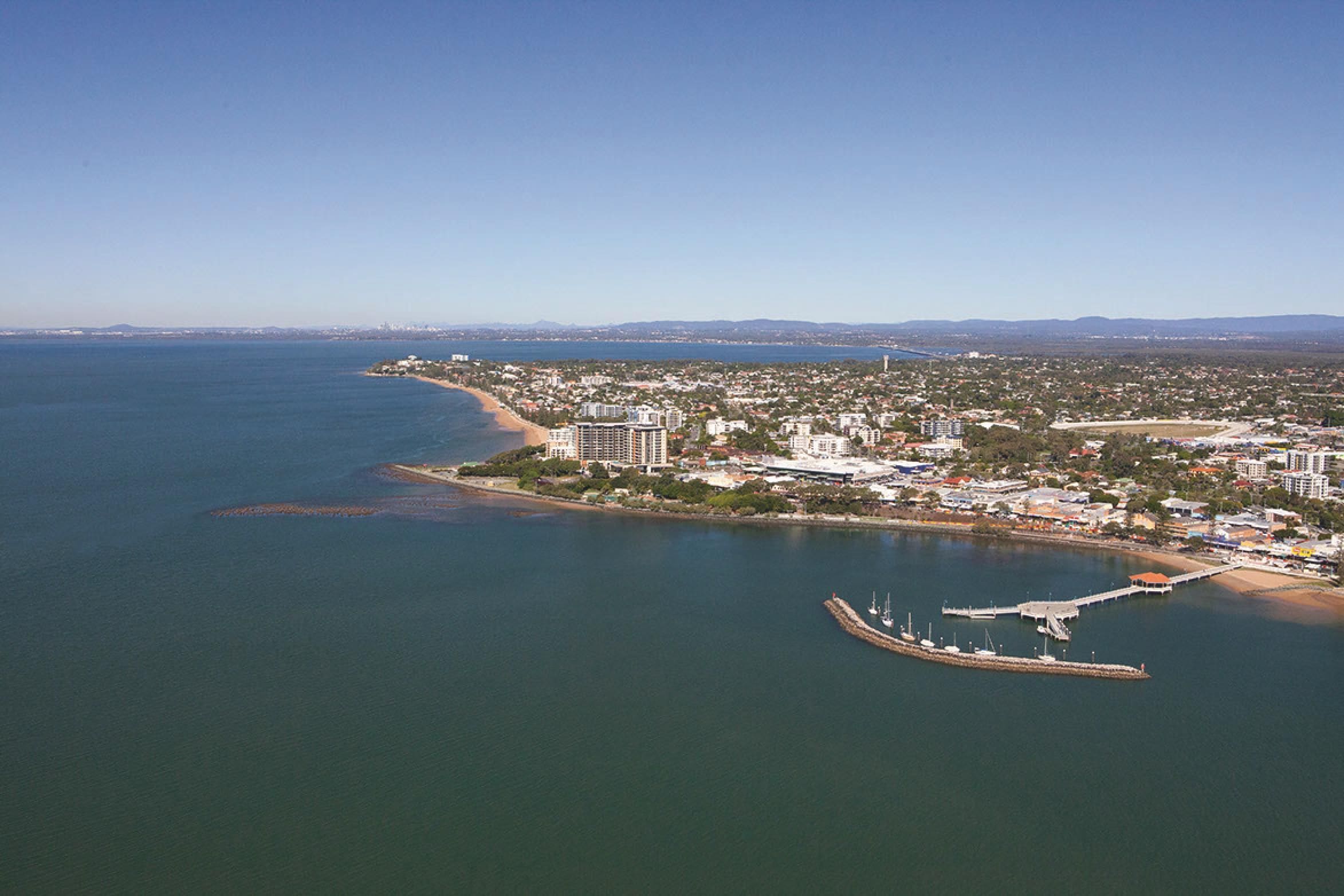 An aerial view of a coastal city with a marina, buildings, and a beach.