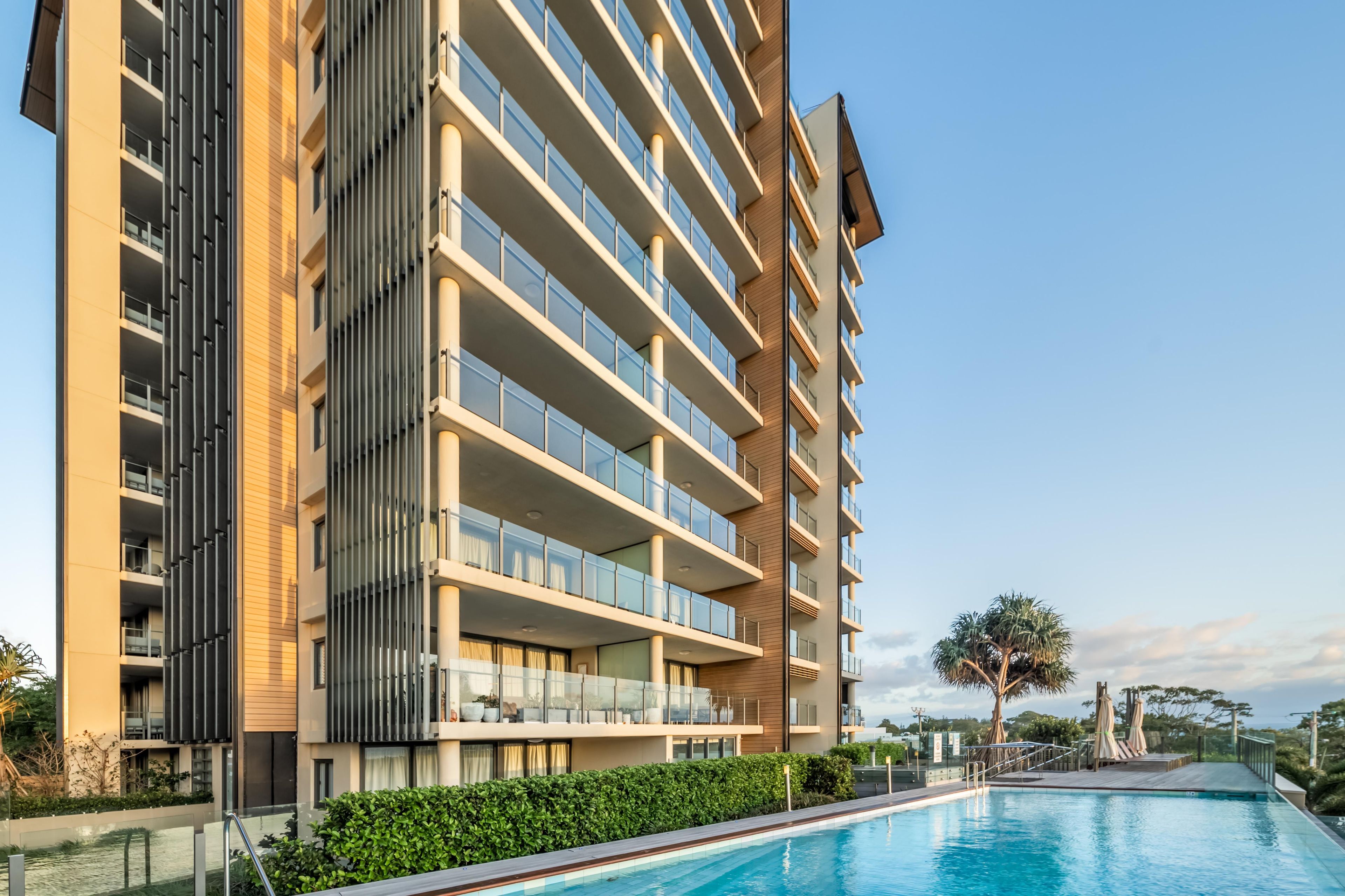 Un moderno edificio de gran altura con piscina, varios balcones y cielo despejado.