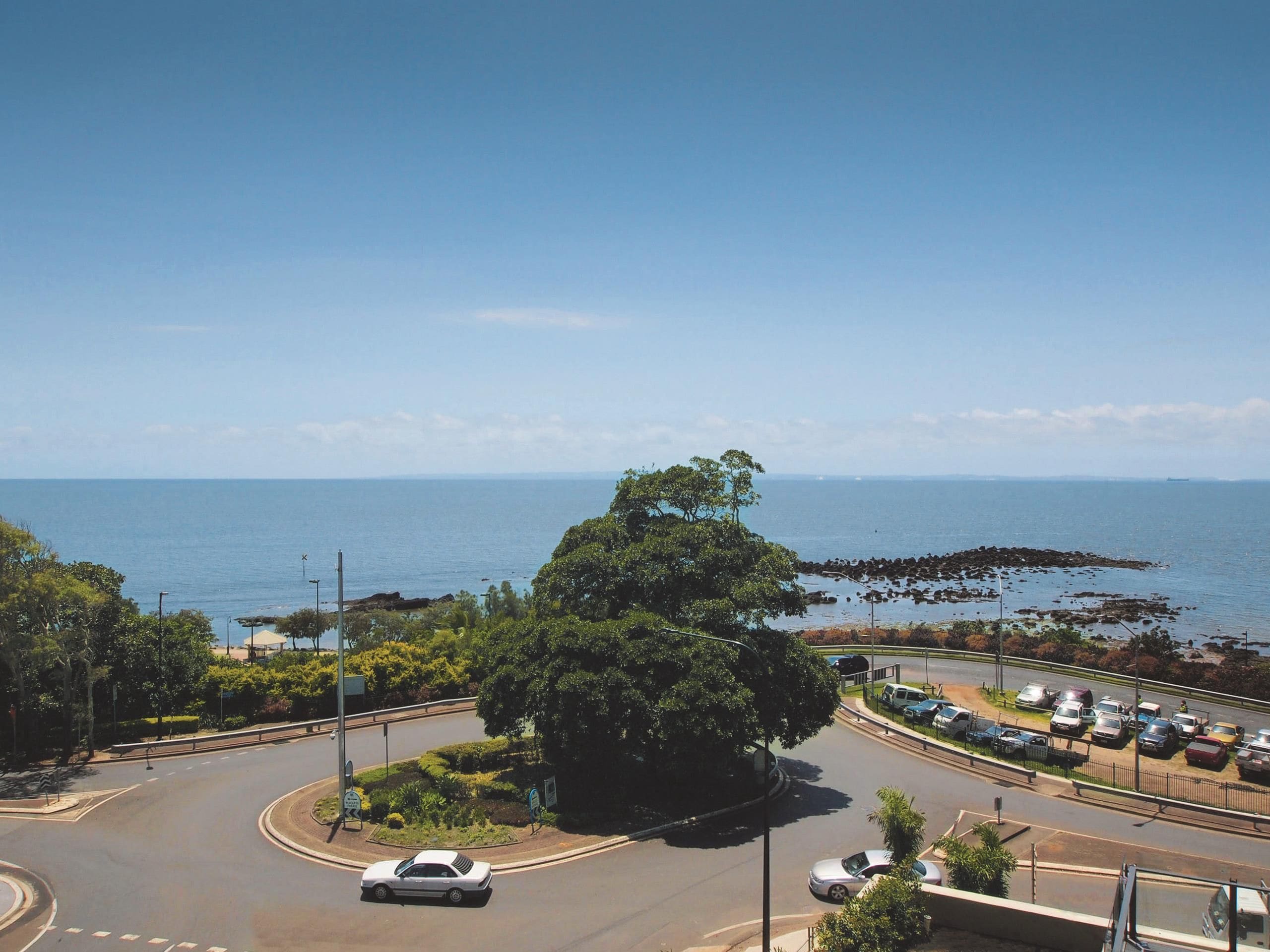 A coastal road with a roundabout, a parking lot, and a view of the sea.
