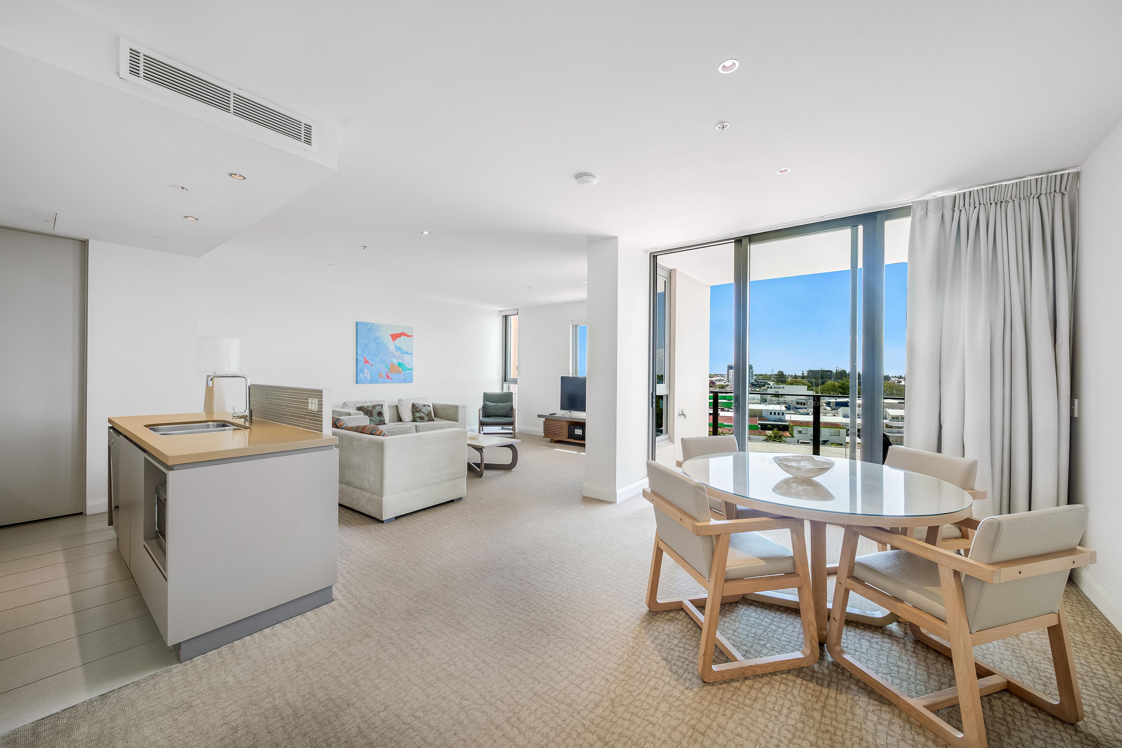 Een moderne hotelkamer met een zithoek, kitchenette en een groot raam met uitzicht op de stad.