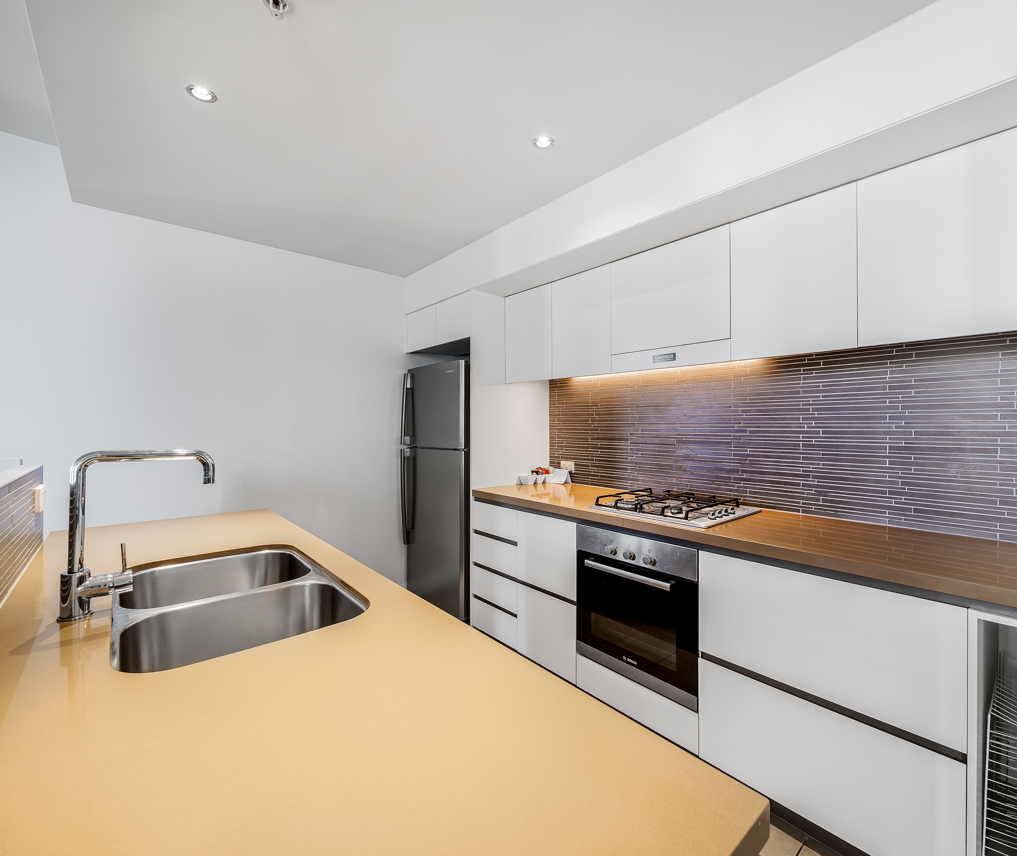 Uma cozinha moderna com eletrodomésticos de aço inoxidável, bancada de madeira e painel de azulejos.