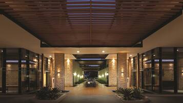 A modern hotel lobby with a wooden ceiling, stone walls, and a central pathway leading to the entrance.