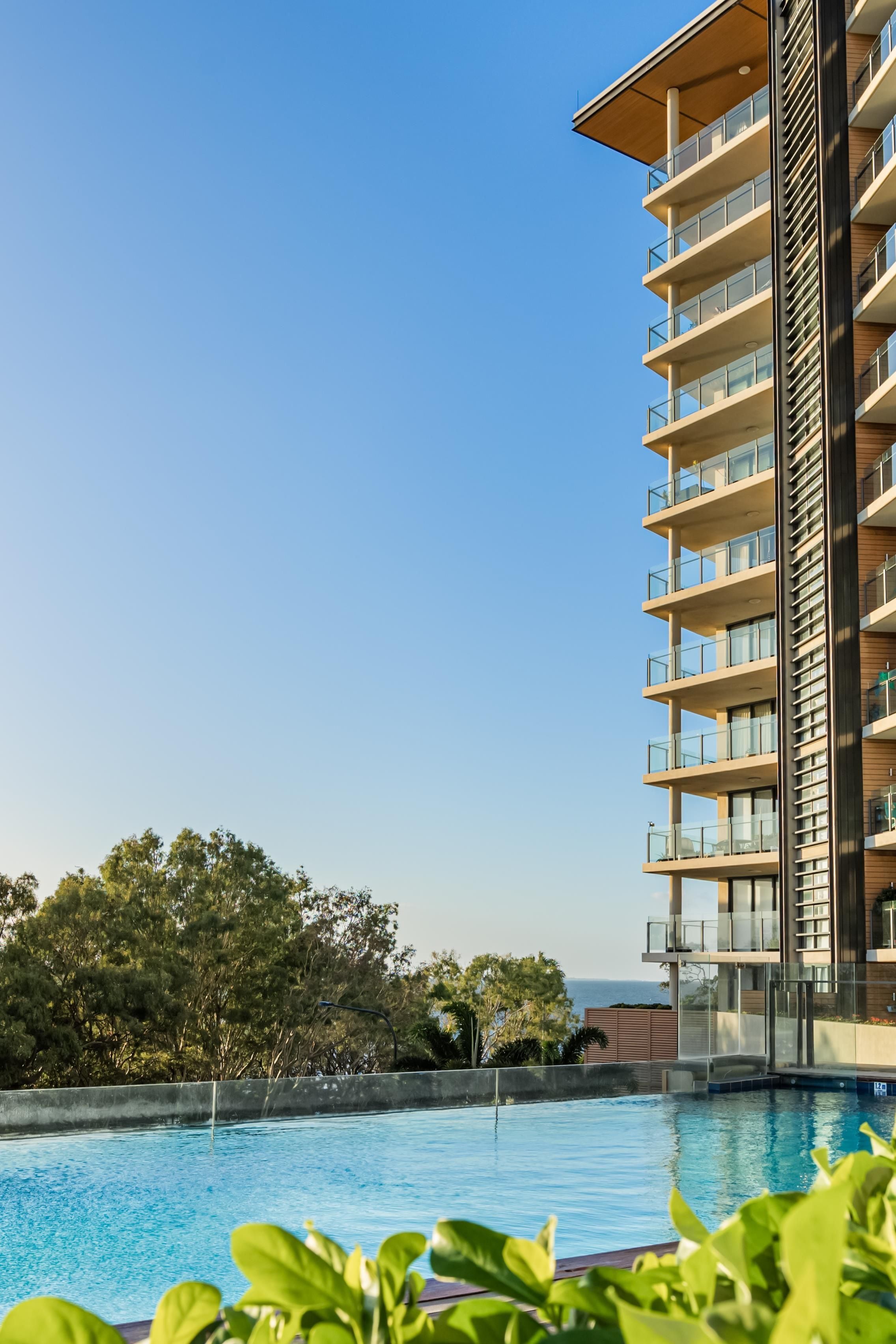 A modern hotel with a pool, multiple balconies, and a view of the ocean.