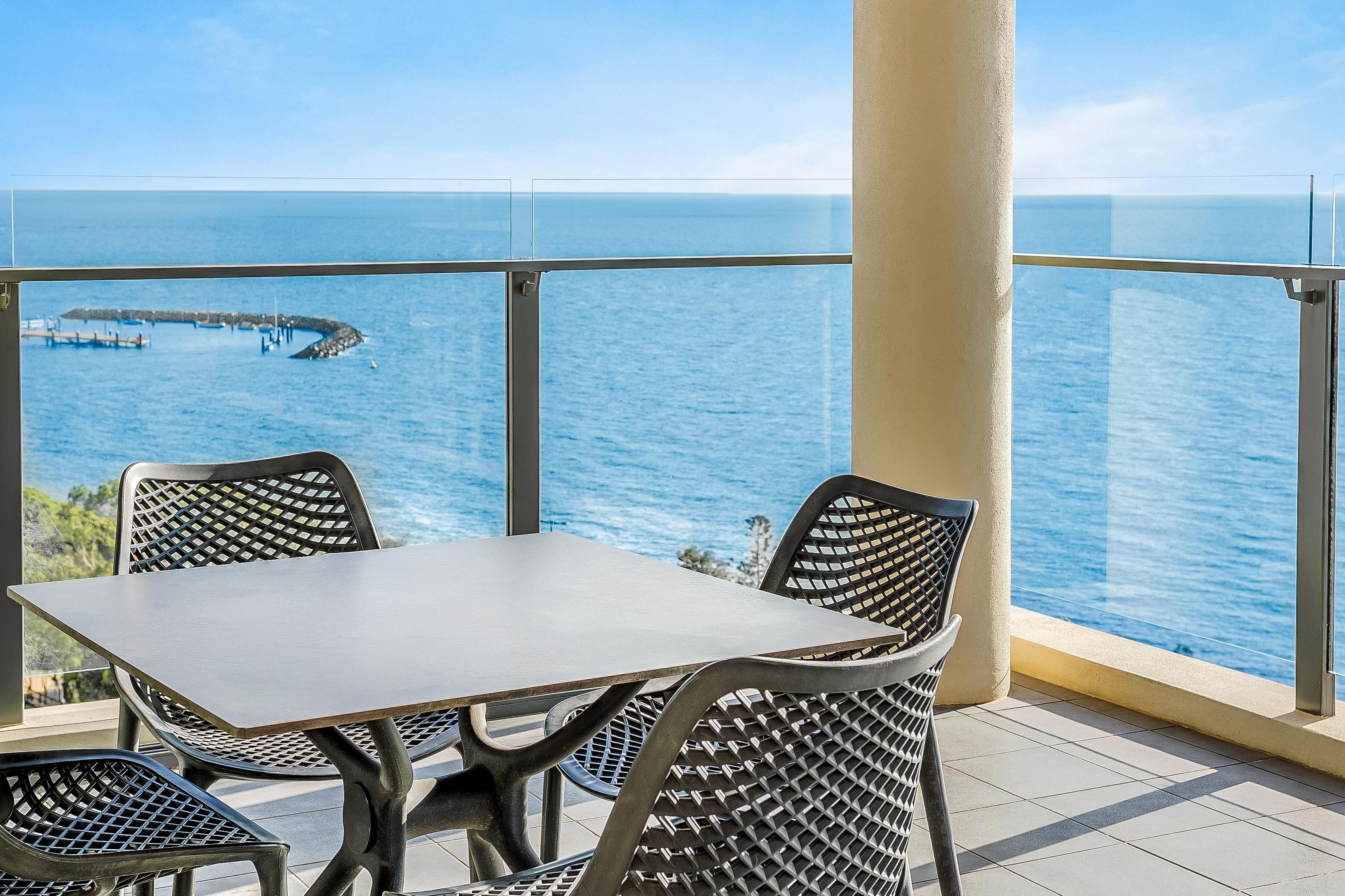 A balcony with a table and chairs overlooking a body of water with a pier.
