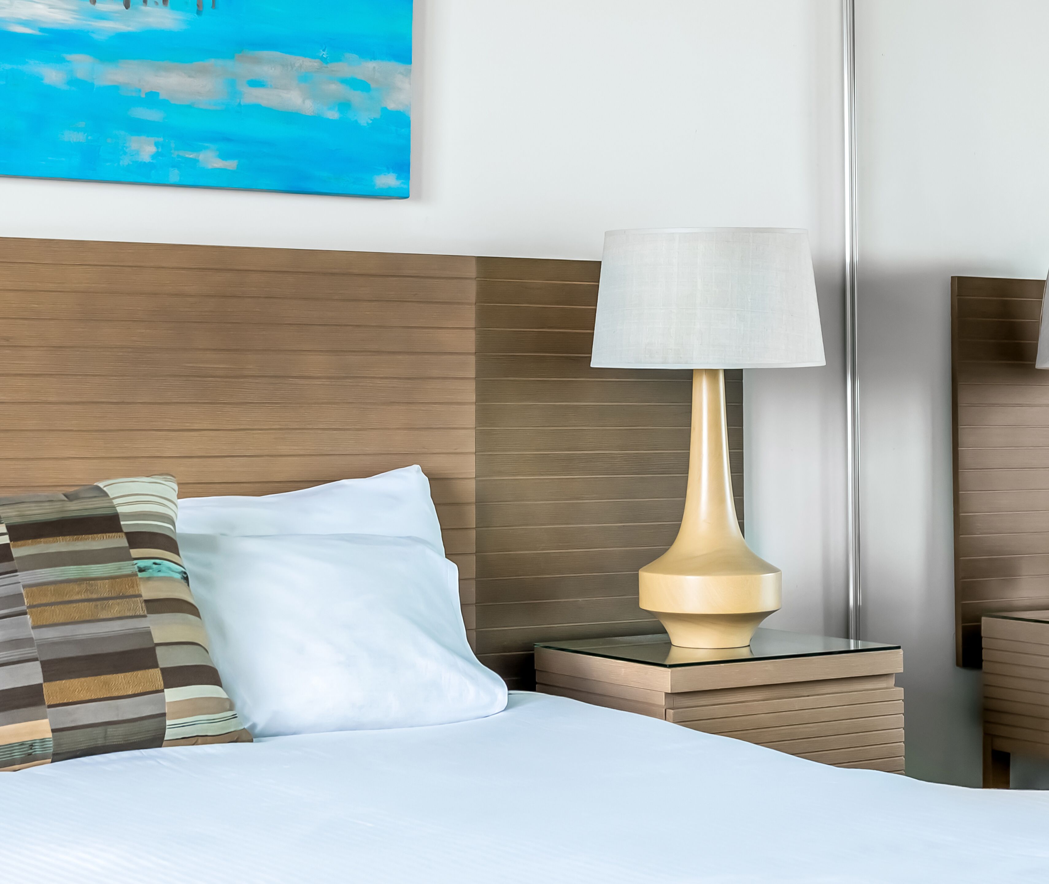 Una habitación de hotel con cama, mesita de noche, lámpara y un cuadro en la pared.