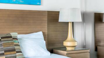 Una habitación de hotel con cama, mesita de noche, lámpara y un cuadro en la pared.