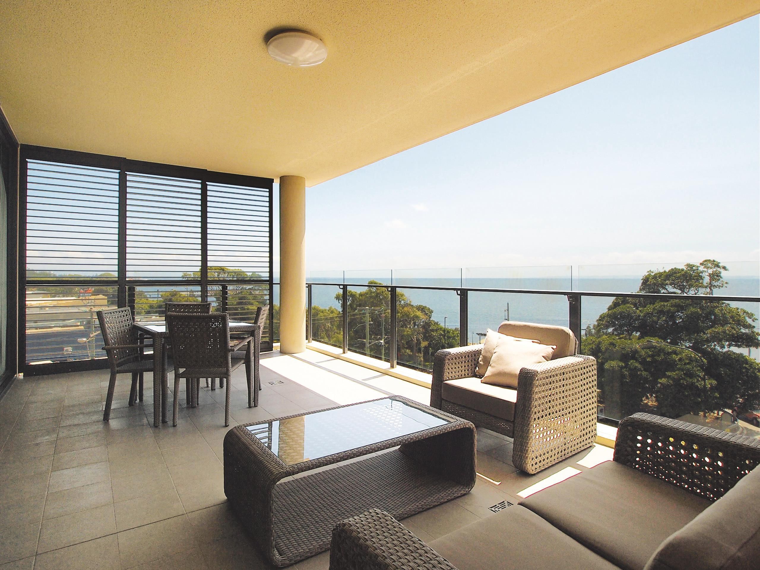 Un balcon agrémenté de meubles en osier, d’une table en verre et offrant une vue sur la mer.