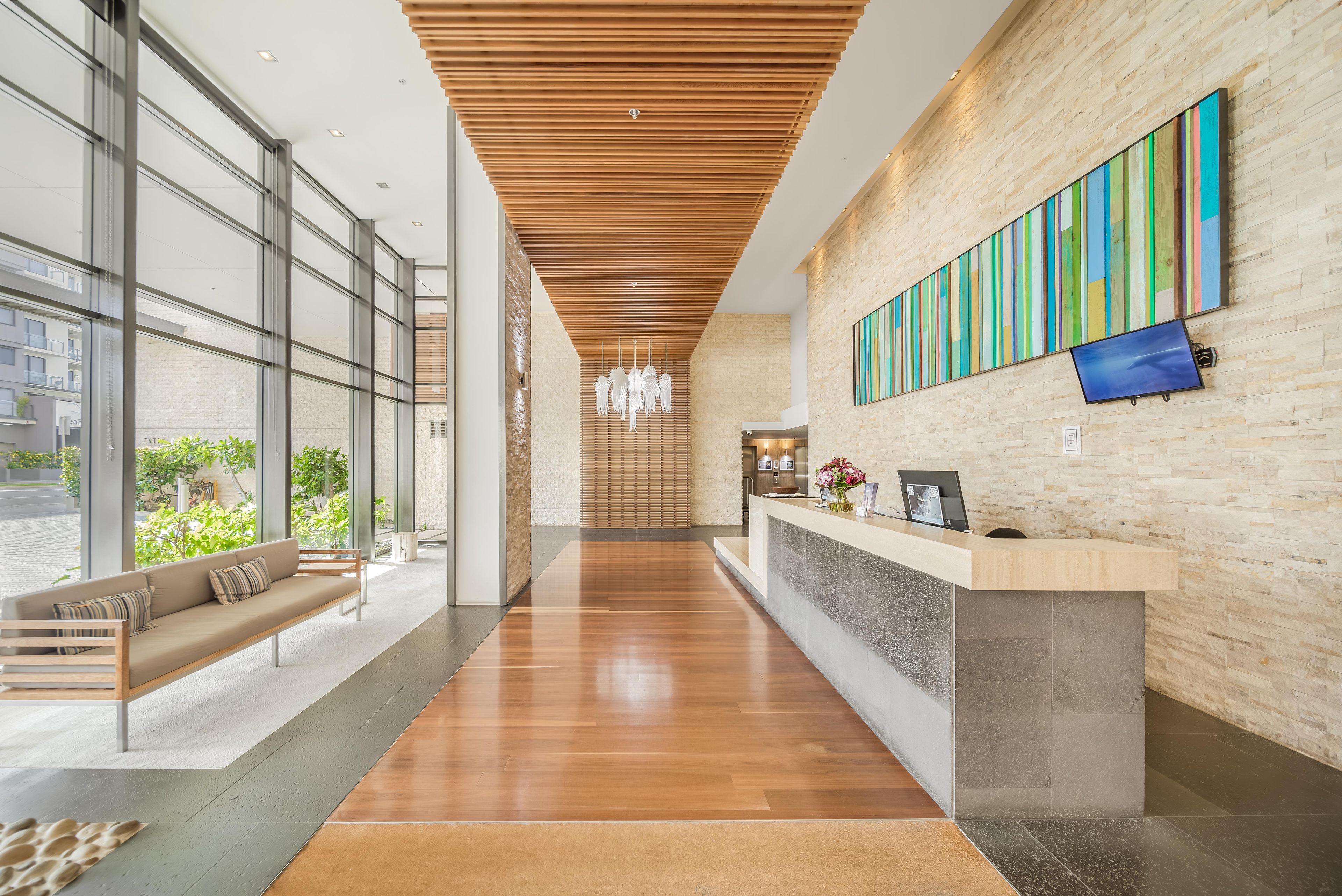 A modern reception area with a wooden ceiling, a reception desk, and a large window offering a view of greenery outside.