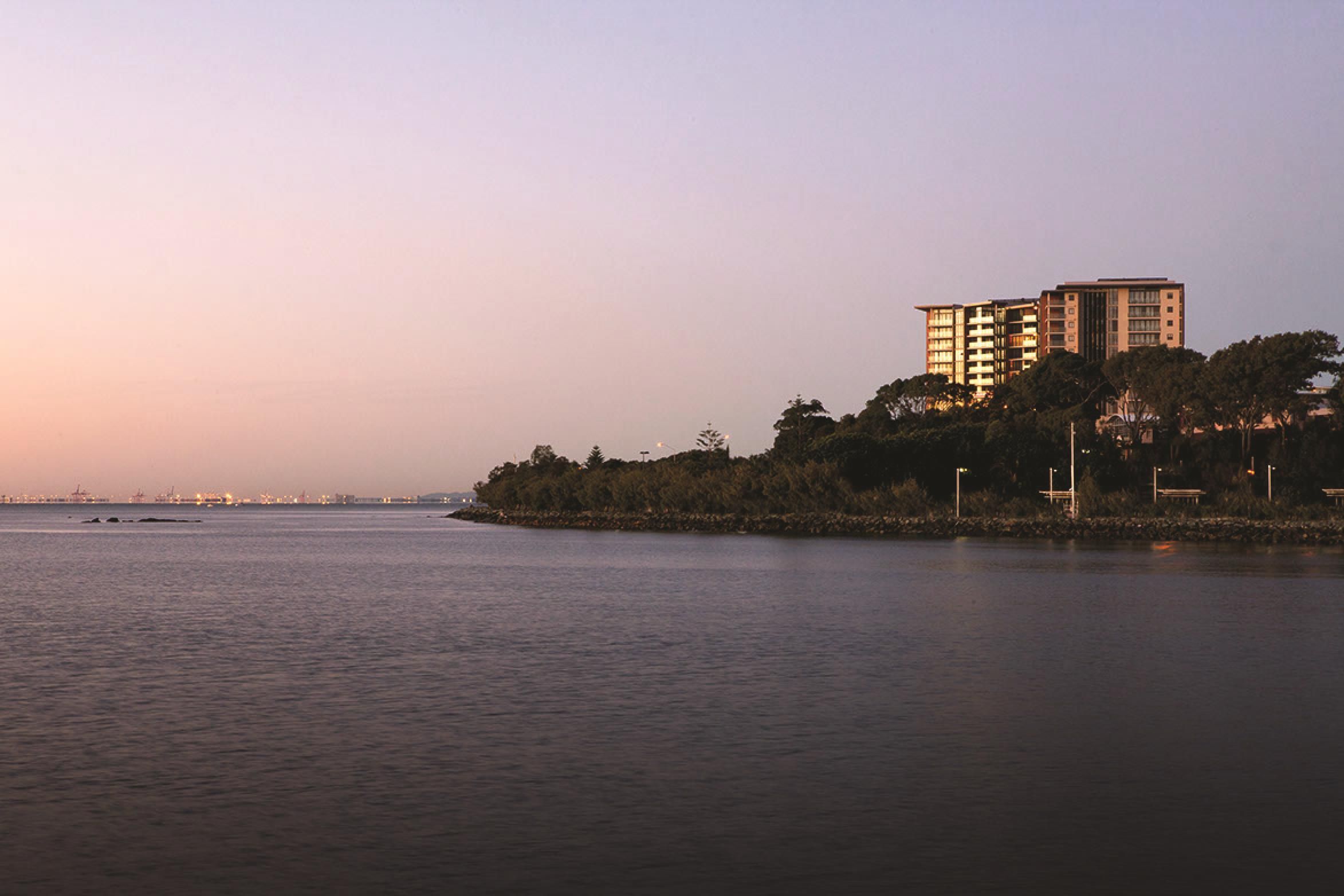A waterfront property with a multi-story building, trees, and a calm body of water.