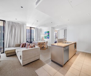 A modern living room with a sofa, dining area, and kitchen. - Oaks Redcliffe Mon Komo Suites (Redcliffe)